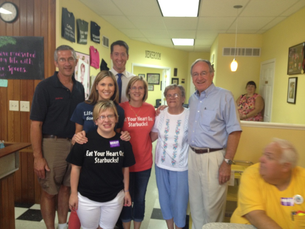 Photograph of Em Lantz and her support team posing inside Em's Coffee Company with former US Senator Tom Harkin