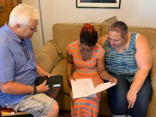 Photograph of Simone Renee Moore, Stephanie, and Daryl sitting on a couch examining papers