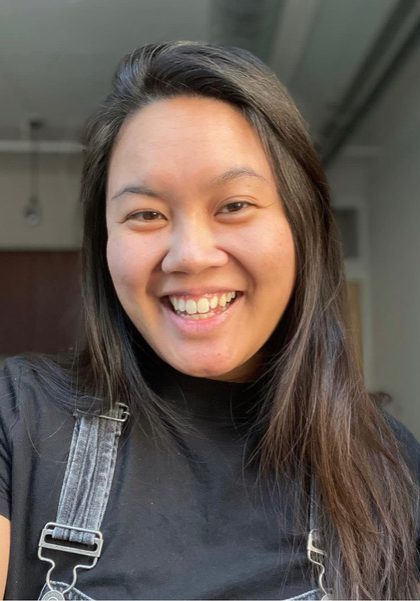 Headshot of Ciara Ladroma. Ciara has long hair, is smiling, and is wearing a T-shirt and overalls.